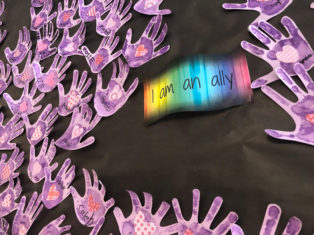 A bulletin board with a rainbow sign that says "I am an ally" surrounded by student handprints of purple paint.