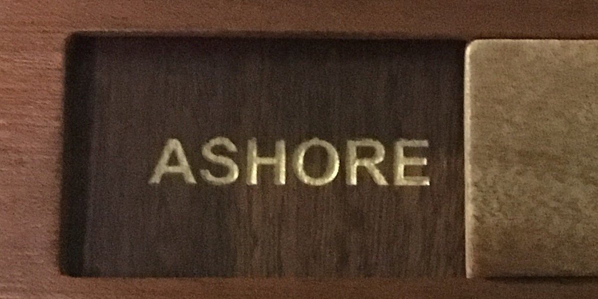 A close up picture of the word ‘ashore’ on a wooden board. It’s to account for people on the ship. Each officer’s job is on a wooden board and every time you come up the gangway you slide your marker to ‘on board’ and as you leave, you move it to ‘ashore’.