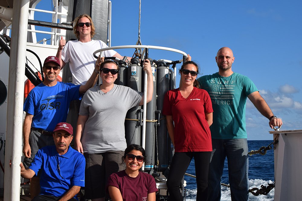 seven researchers standing aboard ship. some wearing Texas A&M apparel