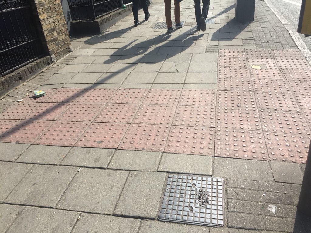At pelican or controlled pedestrian crossings the red bumpy blister paving is in an L shape. The vertical tail of the L connects to the building line. This helps VI people find the crossing as they follow the L into the bottom corner. This also leads to the button box.
