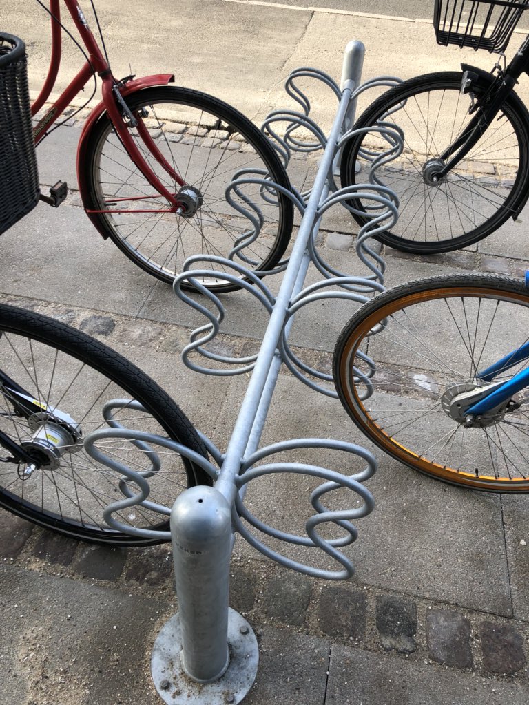 Bike racks. They’re everywhere! They vary in design. They are not an art project, or behind the building, or a design contest for kids, or hard to find. You can park your bike in them and lock it up. Simple. Useful. Everywhere.