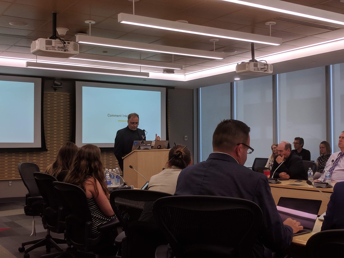 CDS's CEO, Aaron Snow, in front of a podium at the end of a set of boardroom tables. Other attendees are in the foreground, sitting in chairs.