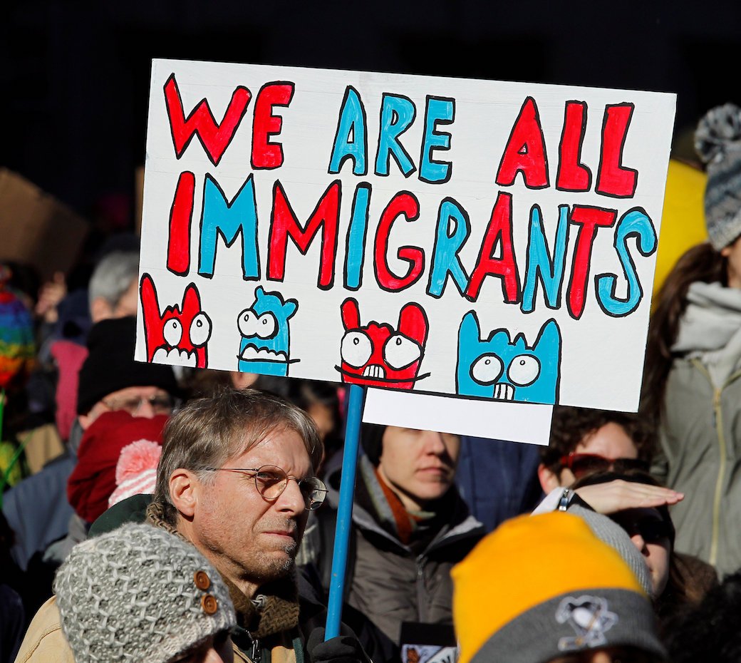 Man in a crowd holding a sign that reads, "We are all immigrants."