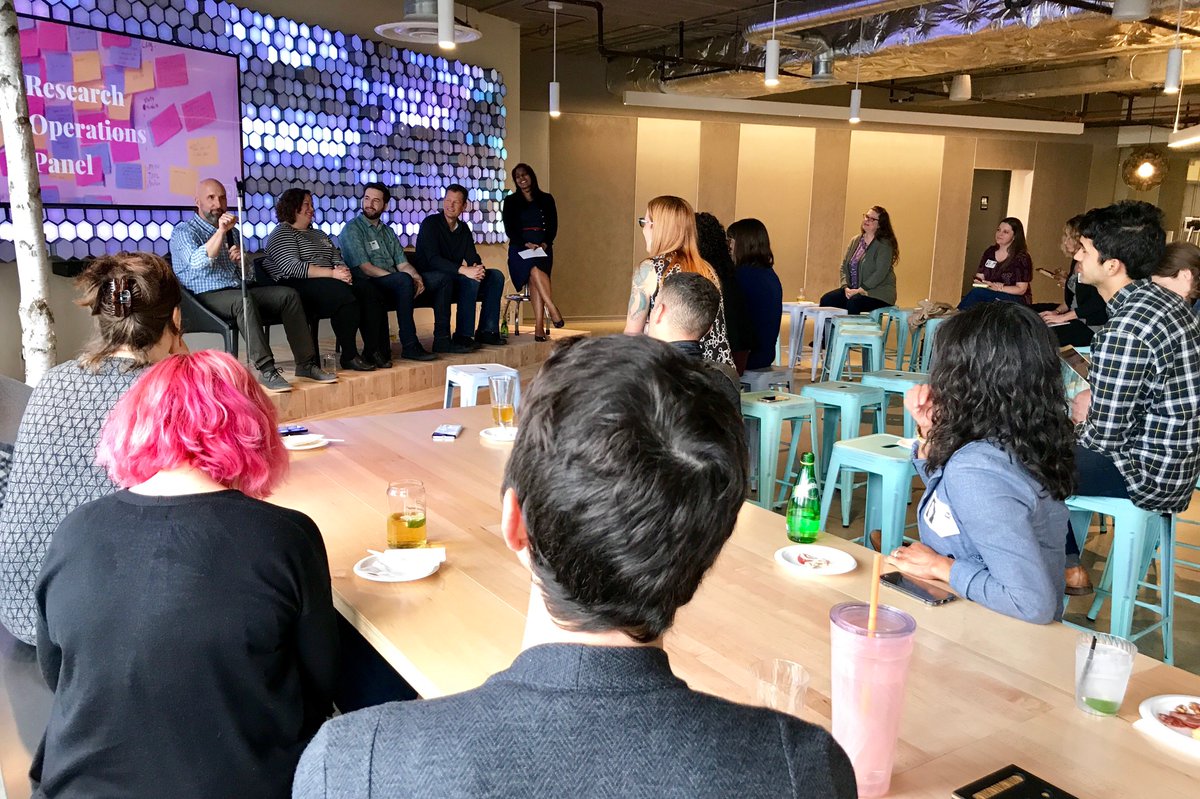 Four panelists and one moderator on stage at Blink, while researchers look on.