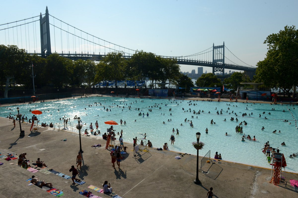 Guests swim and play in Astoria Pool, an outdoor pool by the waterfront and bridge at Astoria Park.