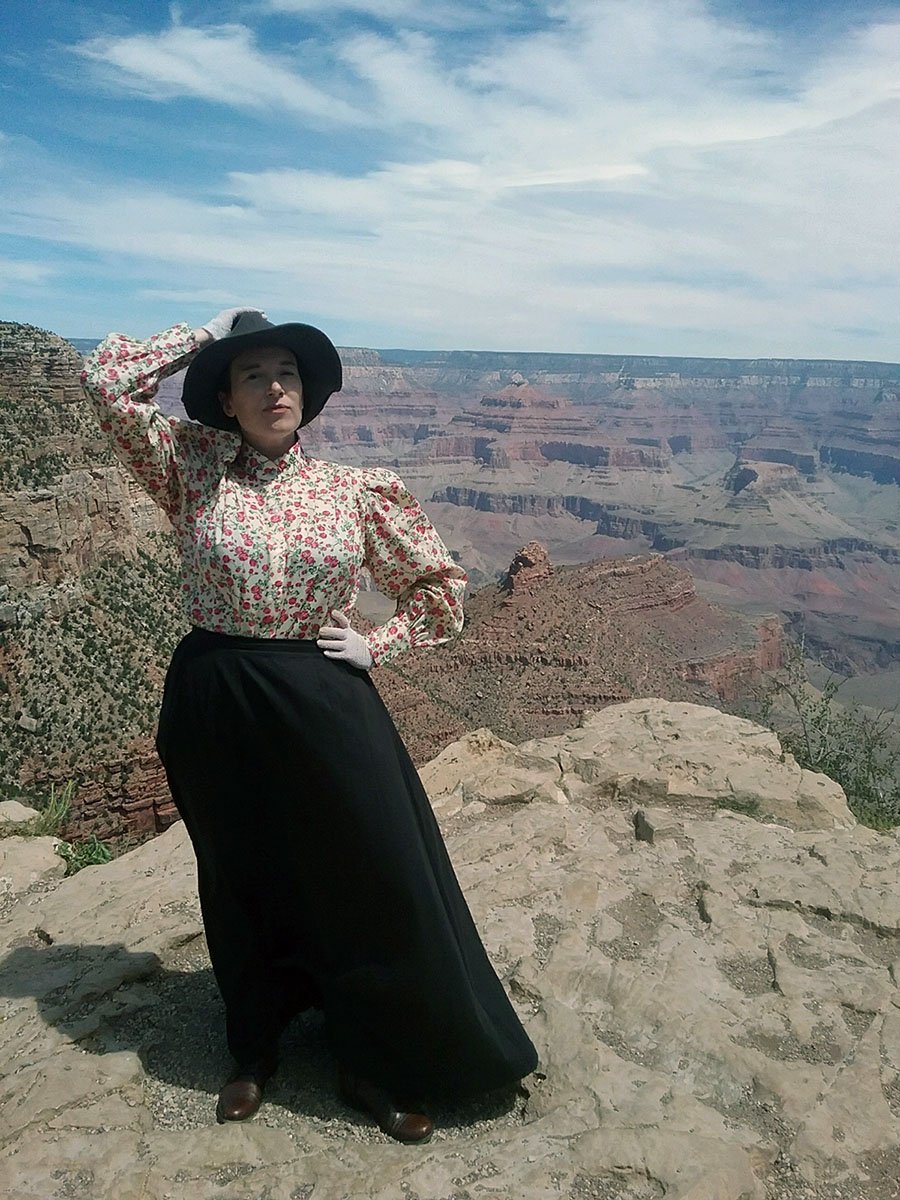 A woman standing in period dress in front of a cliff edge, Grand Canyon in the background