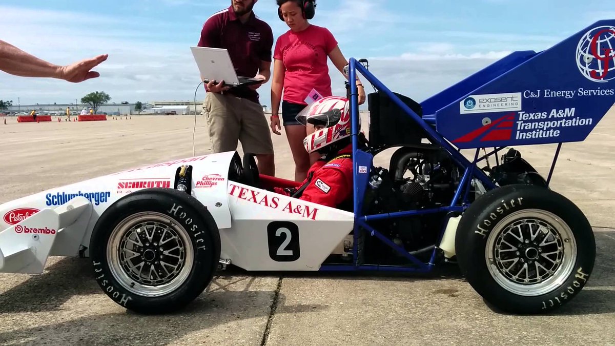 small race car with driver sitting it in and two people standing beside with a computer on a track