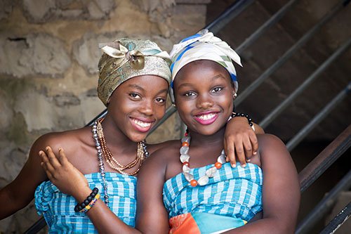 two african teenage girls wearing traditional headresses smiling.