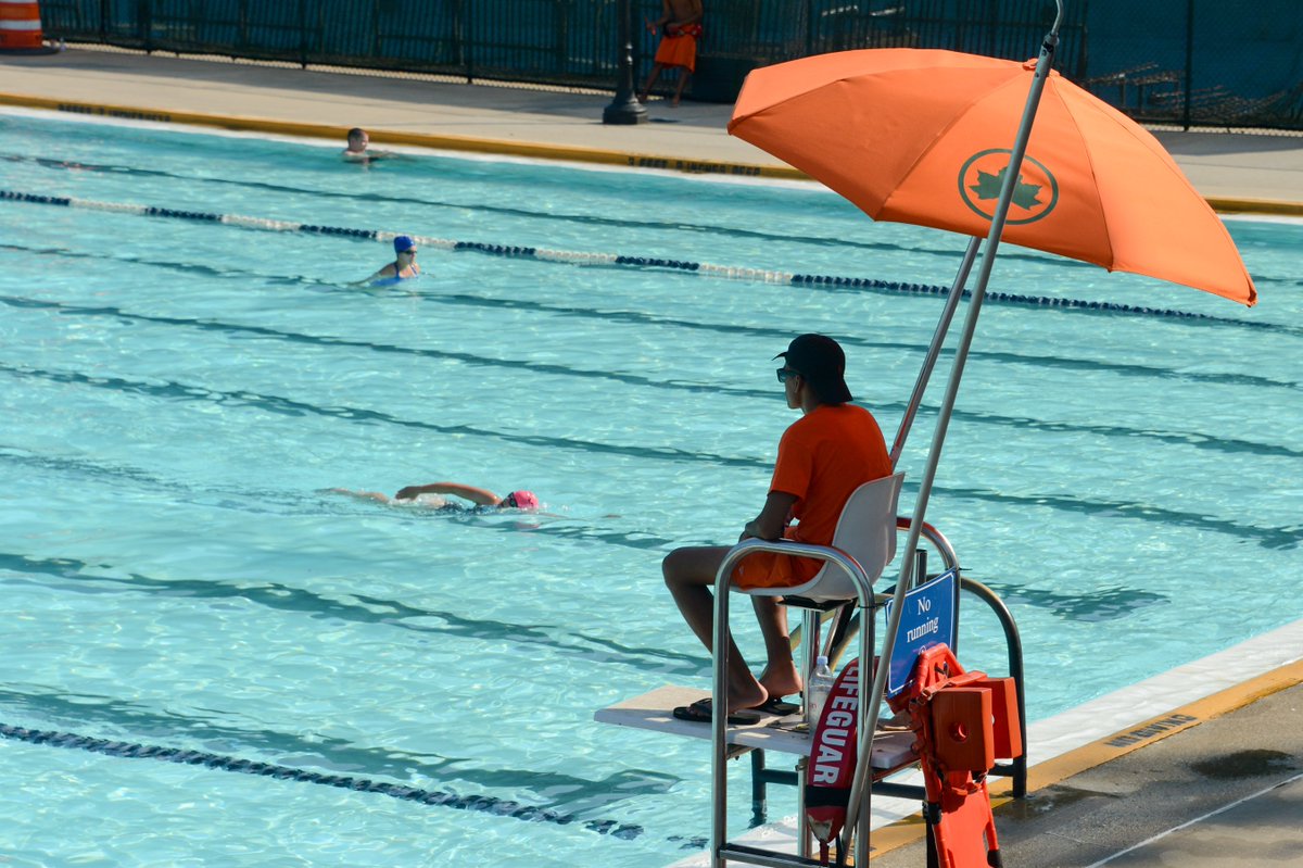 Pool guests swim laps at an outdoor pool with lifeguards.