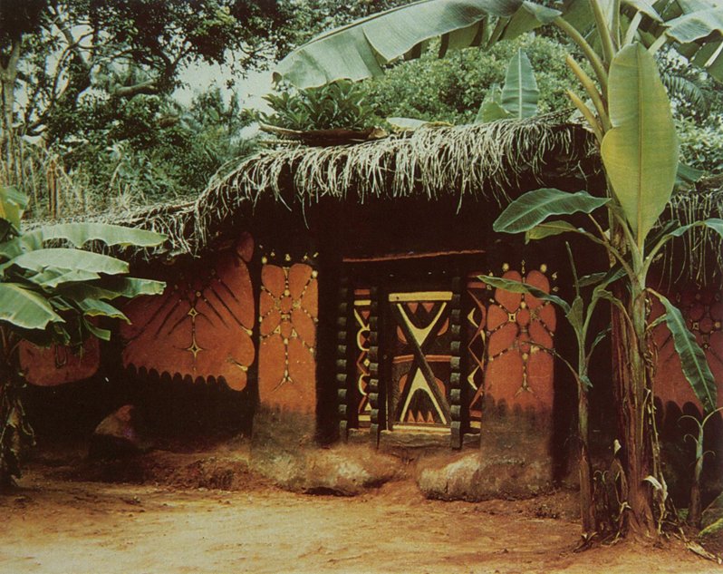 "The entrance to the compound of traditional uli artist Mgbadunwa Okanumme, who decorated her walls for the Asha Olu festival [also known as Afia Olu, a festival usually dedicated to the agricultural divinity Ifejioku]. Nnobi, [northern Igbo area] December 1986." – Liz Willis.