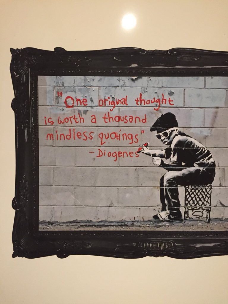 Black-and-white photo of a boy wearing a beret and sunglasses, sitting on a crate against a brick wall and scrawling in red: "'One original thought is worth a thousand mindless quotings' - Diogenes"