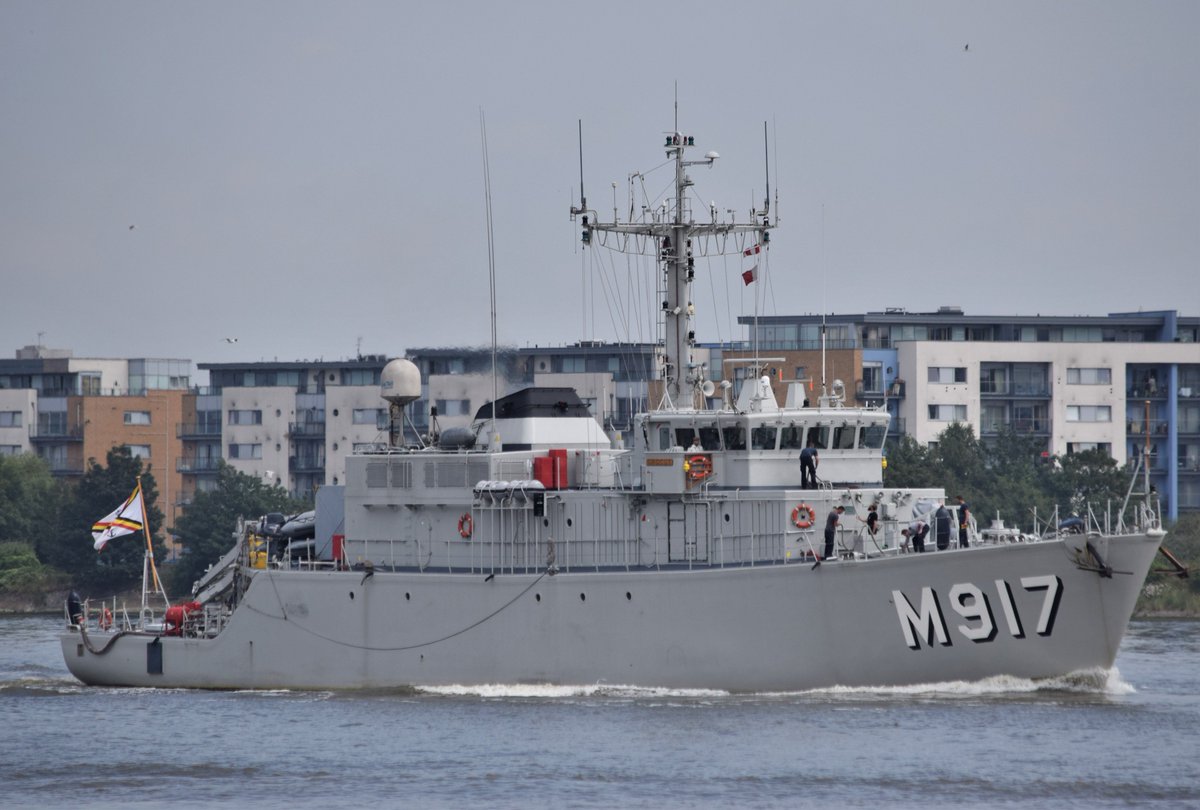 Belgian Navy minesweeper - large M917 code on the bow and flag flying at the stern with sailors preparing ropes on deck