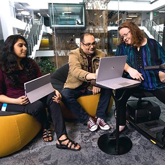 Leith, Chitra and Kathy - 3 microsoft employees sitting in one of our conference rooms working on a their laptops. Kathy is co-chair of our Disability ERG (her scooter is visible), Leith and Chitra are on my team and do awesome stuff!