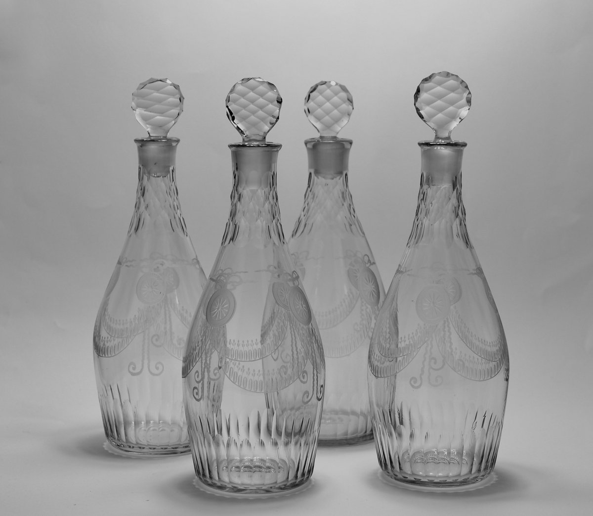 Rare set of four club shaped decanters engraved in the neoclassical manner with roundels, swags of stylised tulips, diamond facet cut necks and cut disc stoppers. English C1770. For sale Art & Antiques for Everyone Summer Fair. #antiquedecanters #18thcentury #marrisantiques