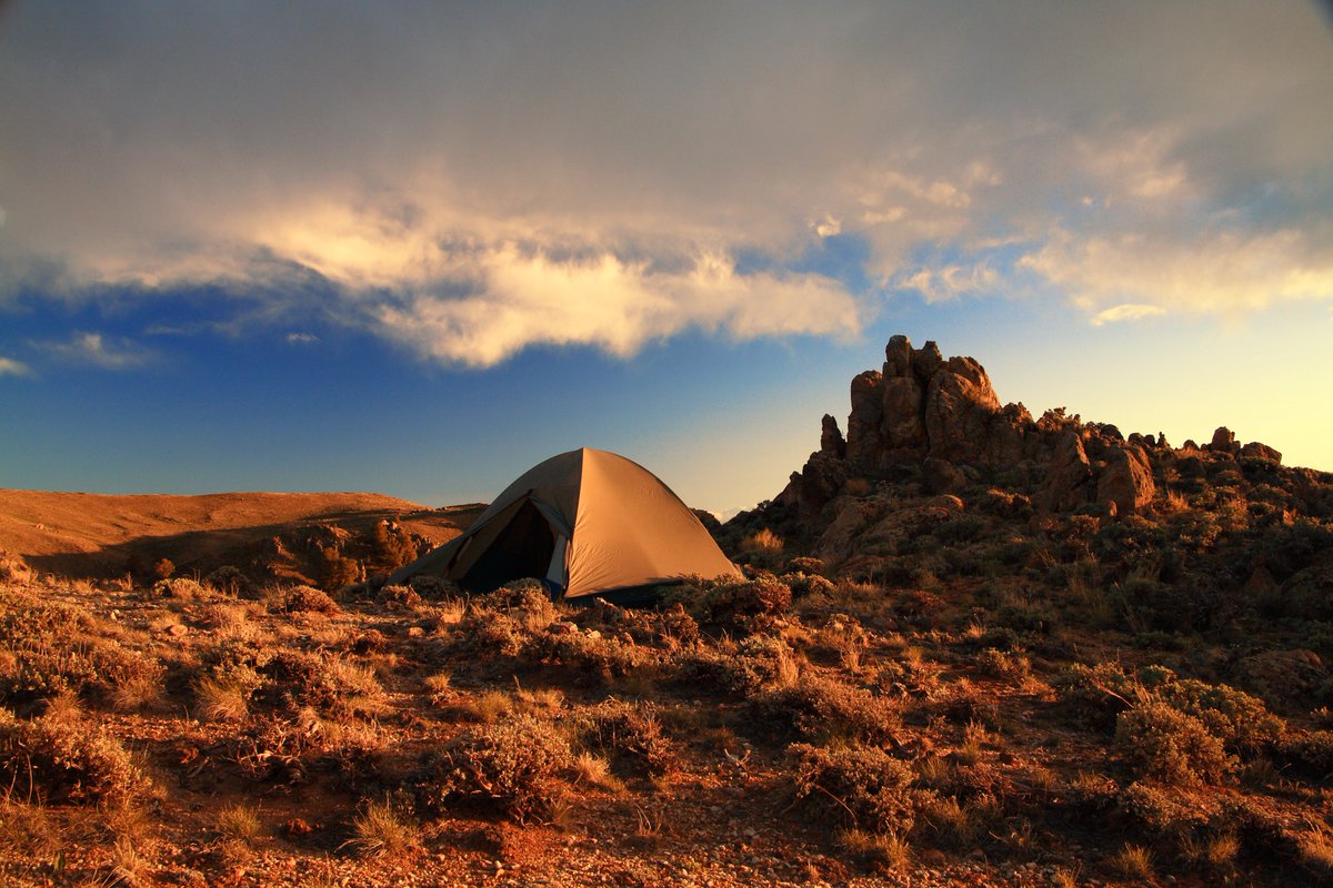 A tent sits on a patch of ground with a rocky outrcop behind.