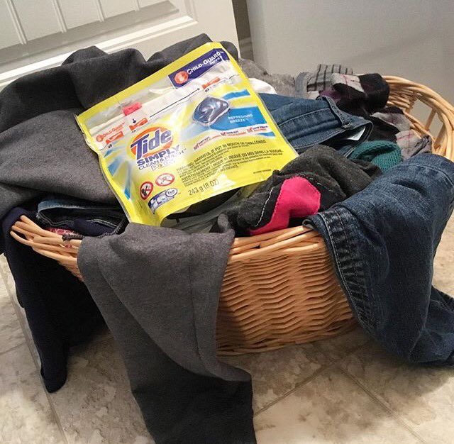 A laundry basket filled with clothes and a package of Tide pods on top.