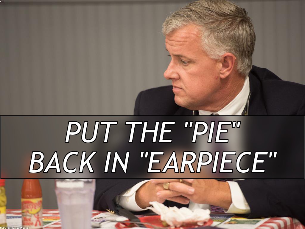 A man in a suit and tie has his hands folded in front of him, he's looking to the side, apparently concerned