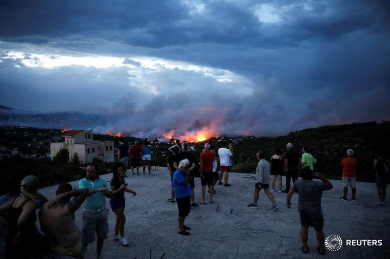 People watch a wildfire burning in the town of Rafina