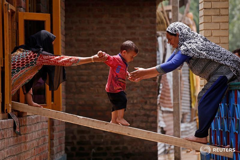 Women help a child to cross over to another house on a wooden plank after flash floods on the outskirts of Srinagar