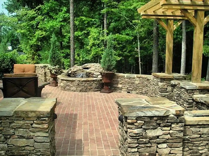 DreamYardTeam's tweet photo. A manufactured brick #patio surrounded with natural stone pillars and walls. A #waterfall spills into a beautiful round #stonepool. This well planned and profession-ally built project also includes built in lighting and drain holes. #landscaping #hardscape https://t.co/fDr5NEFONK