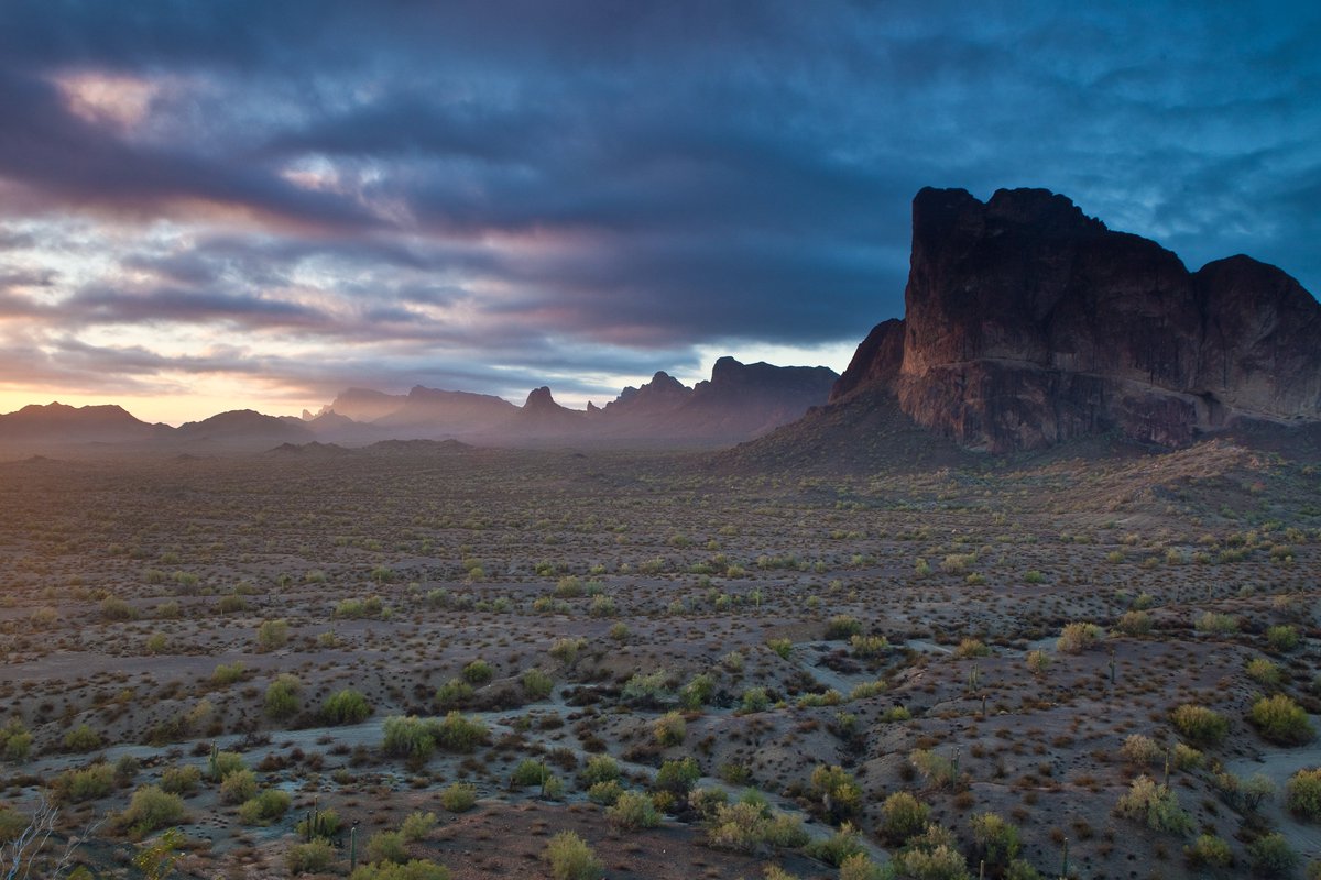 A line of rocky mountains stand on the edge of a desert plain at sunset.