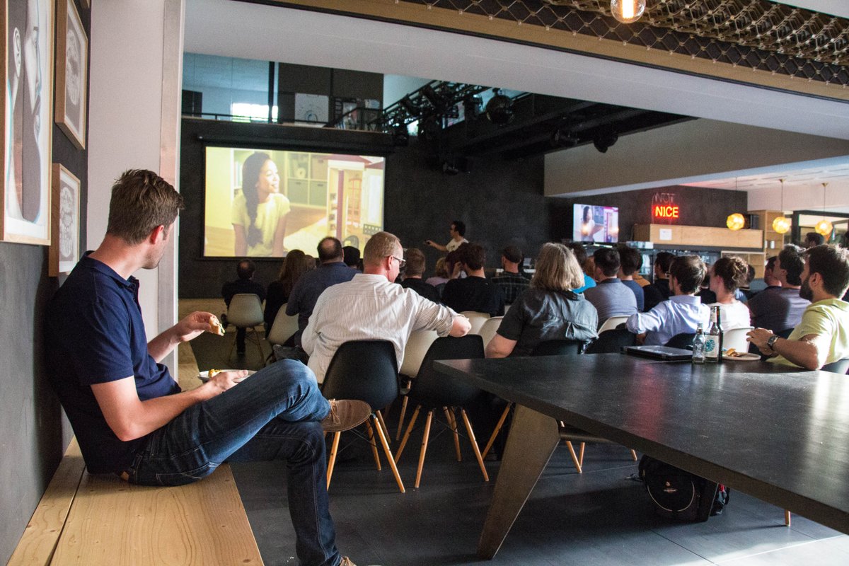 Blick von hinten auf einen großen Raum, gefüllt mit Teilnehmern, die einem Vortragenden und seinen projizierten Slides aufmerksam folgen.
