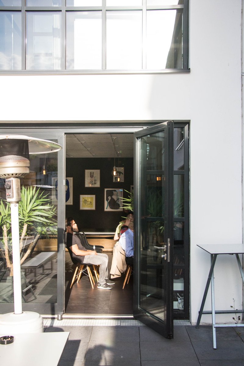 Blick durch offenen Türen in den Vortragsraum - von außen scheint Sonne auf das Gebäude, innen sieht man aufmerksam lauschende Teilnehmer