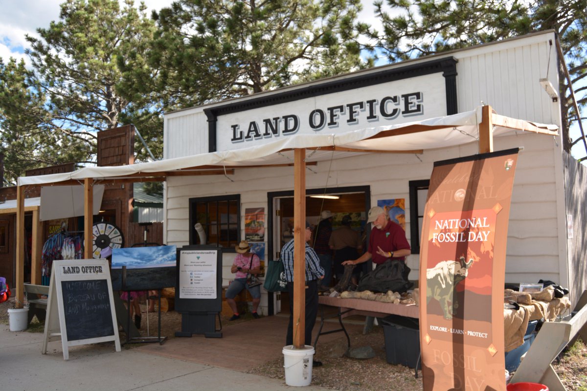 A small white building that says LAND OFFICE with an awning and people in front.
