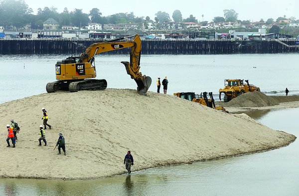 A work crew deploys heavy equipment Wednesday morning to breach a stretch of beach to release water from the San Lorenzo River out to sea. Typically, each year sand builds up and blocks the river from flowing to sea. The crew worked about four hours to open a new channel.