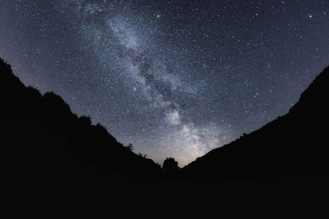 milkyway stripes the sky through a silhouetted valley