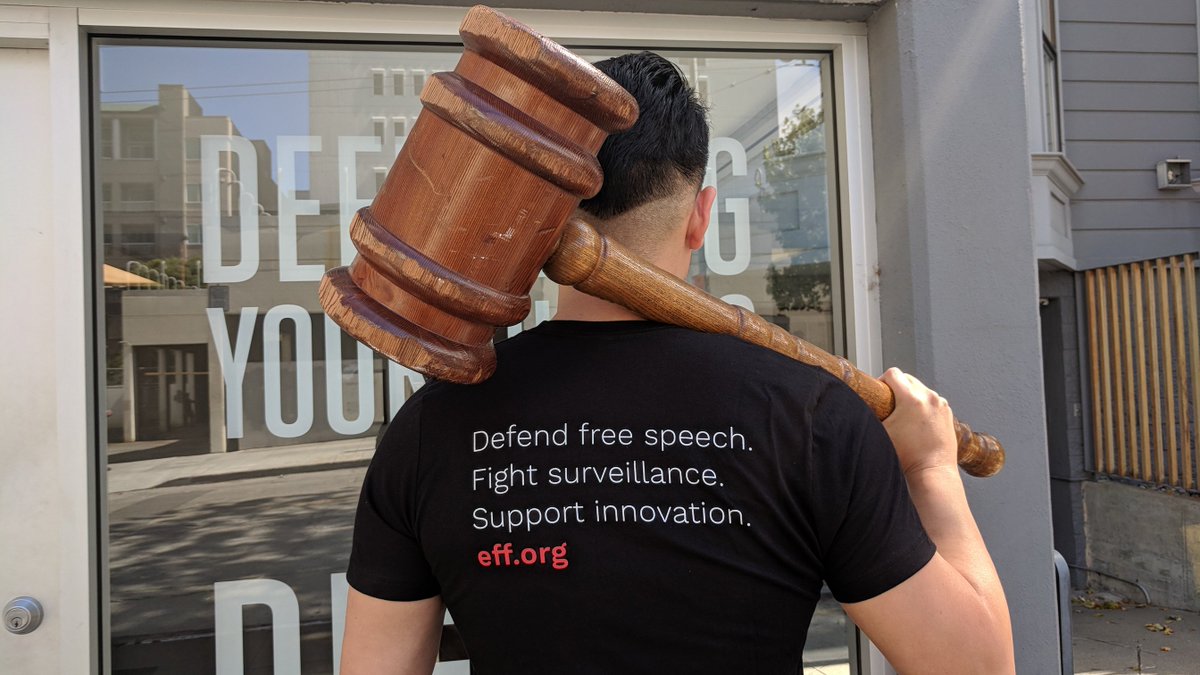 A person holding an oversized gavel facing away from the camera. The back of his EFF shirt says "Defend free speech. Fight surveillance. Support innovation. eff.org."