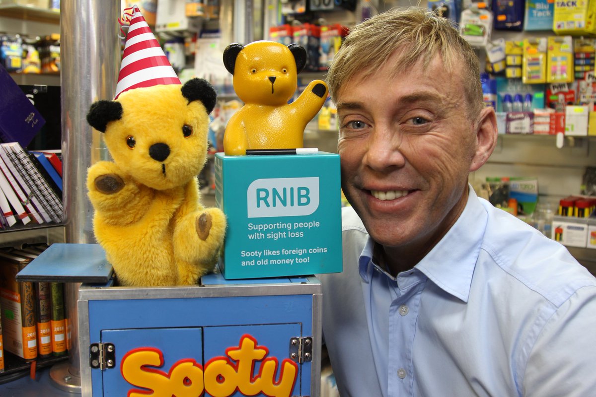 Sooty with a birthday hat on beside an RNIB Sooty Collection Box and presenter Richard Cadell