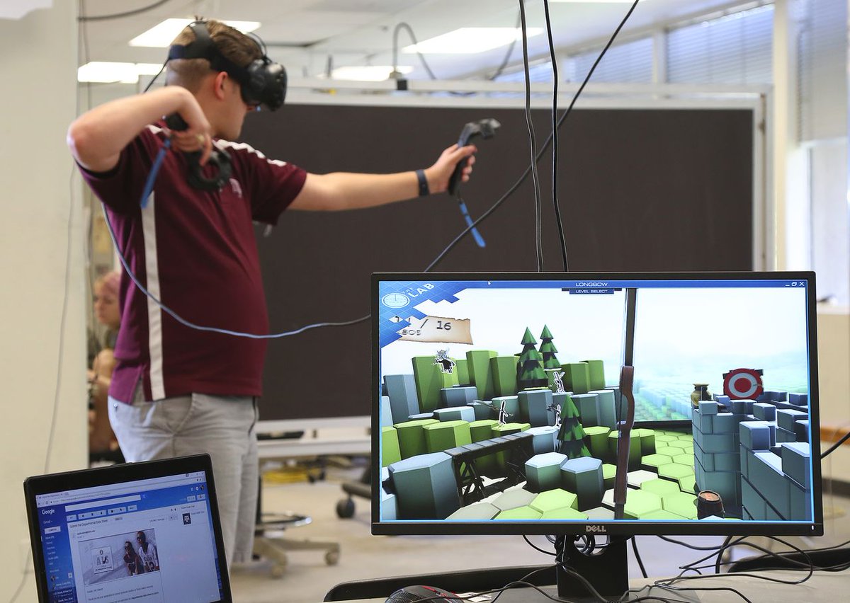 Student in Texas A&M polo with vr headset playing game with computer screen showing game