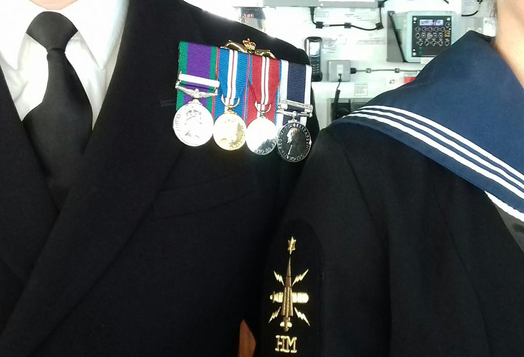 A heavily cropped image of an officer and a rating in number one uniforms - medals, sailor's collar, dolphins, HM branch badge