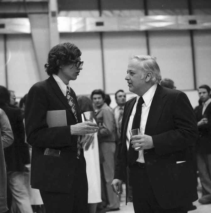 Black-and-white photo of two men wearing suits and holding drinks in their hands at a party