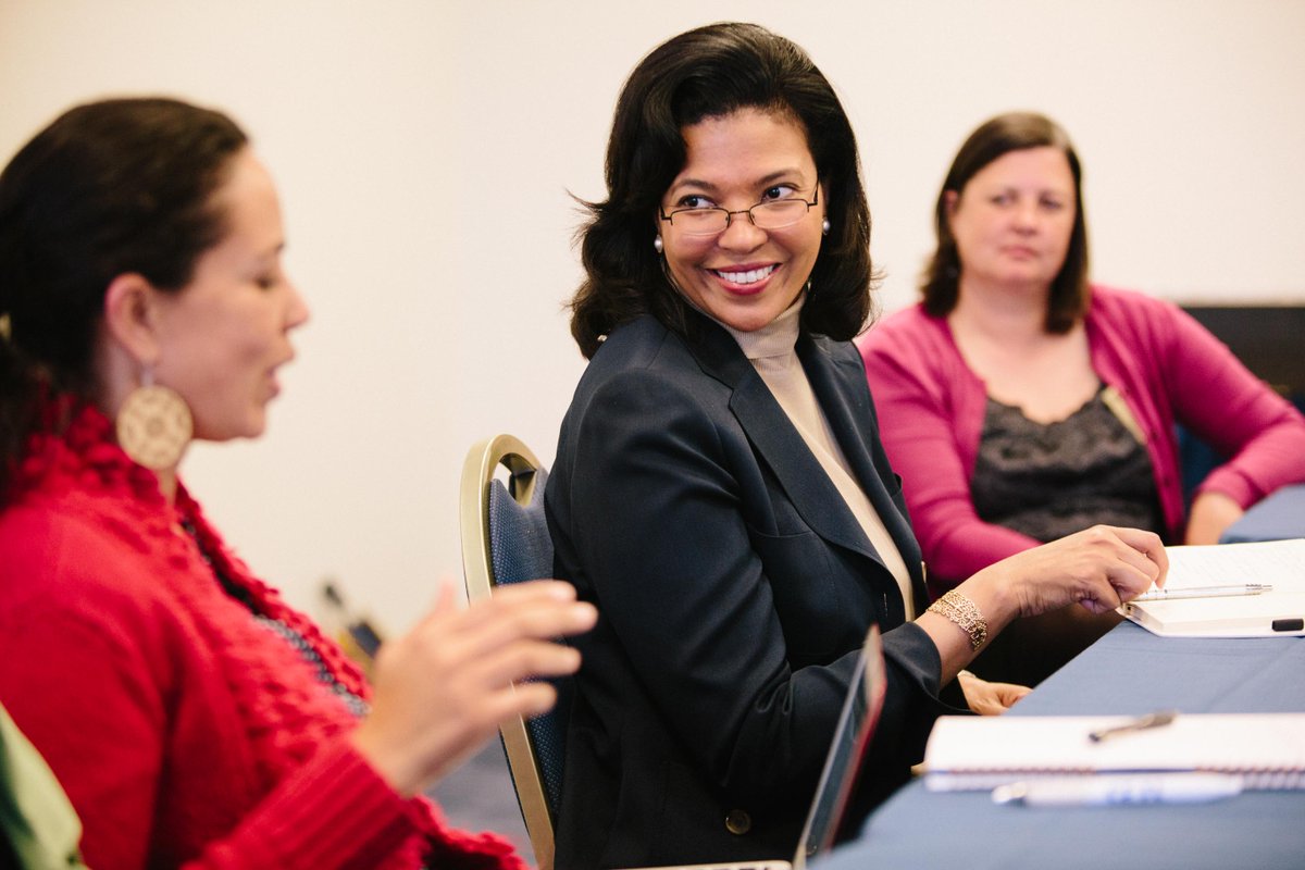 Kim Hunter Reed, seated, turns and smiles at someone during a meeting.