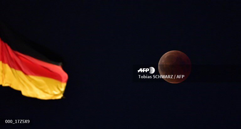 The total lunar eclipse is picutred next to the German national flag atop the Reichstag building, seat of the German lower house of parliament Bundestag in Berlin on July 27, 2018.  #EclipseLunar #AFPphoto #AFP