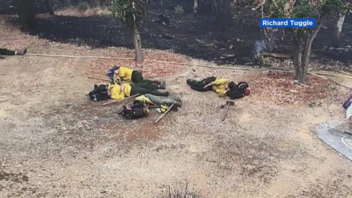 ABC7's tweet photo. #CarrFire firefighters nap in burned-out Redding yard after saving house https://t.co/e3YpVnTJnP https://t.co/TYSvHGuJxE