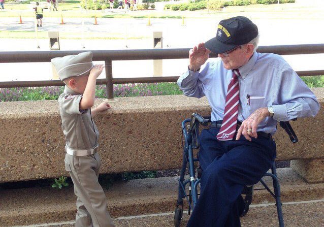 Ike Morris in seated saluting a young boy dressed as a cadet