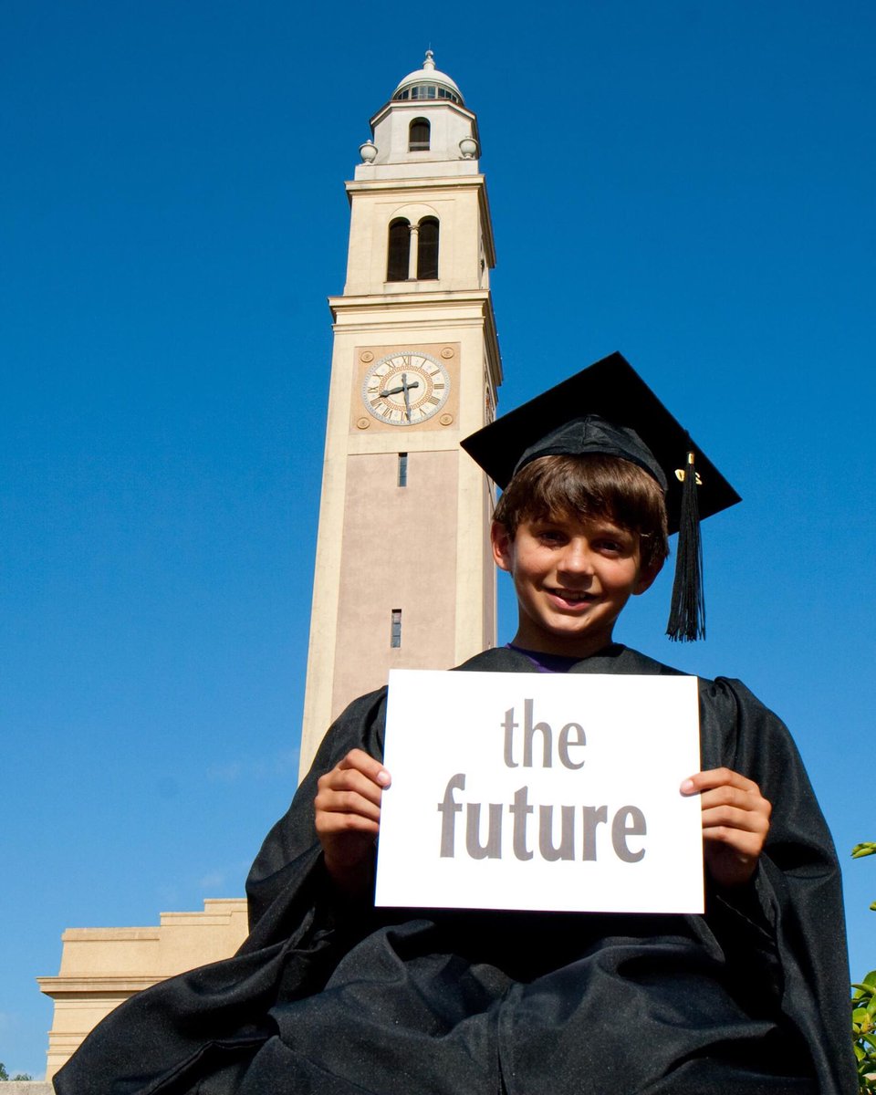 Incoming student Dalton at 10 years old holding up a sign saying "the future" while wearing a cap and gown outside of Memorial Tower.