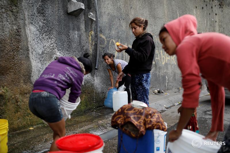 Women fill containers with water coming from a mountain, in a road at Plan de Manzano slum in Caracas, Venezuela