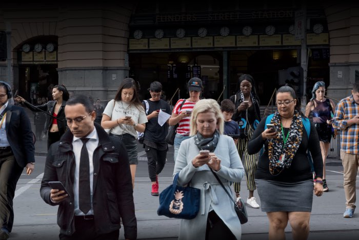 People crossing the road outside Flinders a Street Station ... we are addicted to our devices