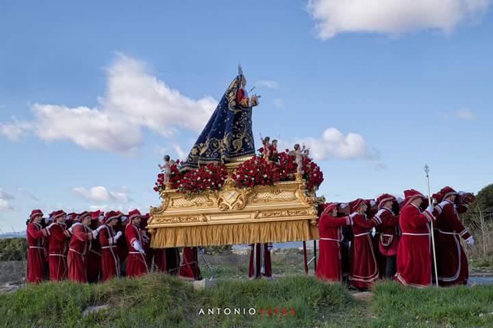 Bajo tu manto me amparas cada día del año, y llevo por bandera tu túnica escarlata bajo el sol de la mañana que inunda tu cara de un amor infinito, hacia la colina hellinera.
