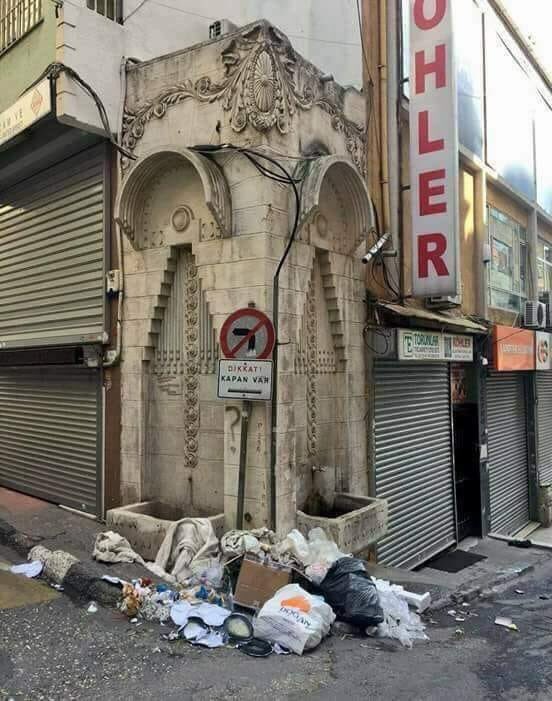 Bu fotoğrafta kimi eleştirelim şaşırdık. 
1-Telefon kablolarını çeşmeye döşeyen TELEKOM'u mu,
2-Çöpü toplamayan BELEDİYE'yi mi,
3-Çöpü döken MAHALLELİ'yi mi, 
4-Levhalarını oraya asan TRAFİK Şubeyi ve Esnafı mı
5-Bitişiğine o çirkin balkon projesini onaylayan İmar Müd.’nü mü?