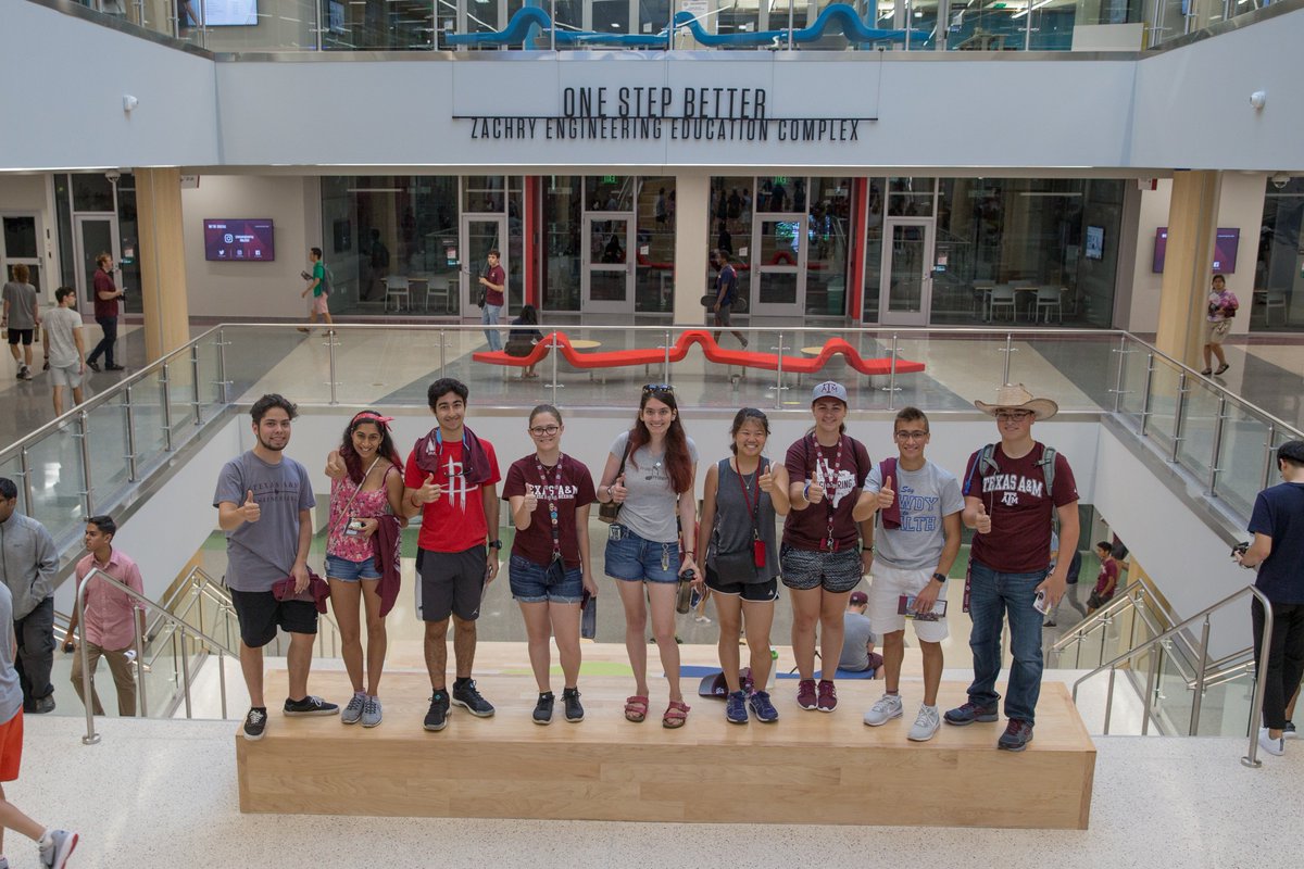 Nine Aggies standing on stairs with their thumbs up