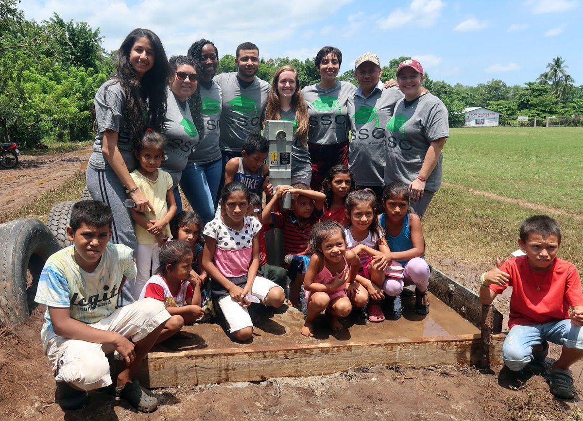 Eight SSC workers and students taking a photo with children and a water well