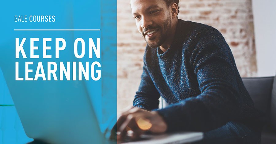 a photograph of a Black middle aged man smiling as he works on his laptop