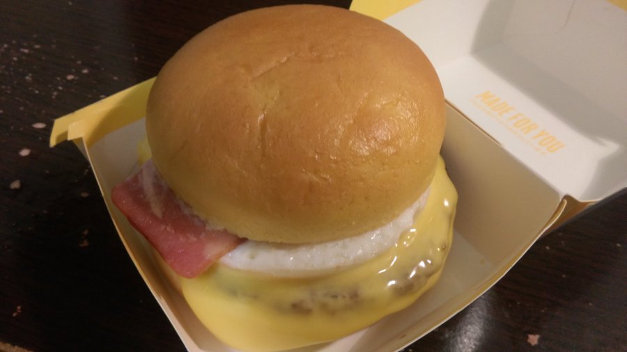 A photograph of McDonald's Tsukimi Burger, which is a bacon cheeseburger topped with a fried egg and a golden, seedless bun.