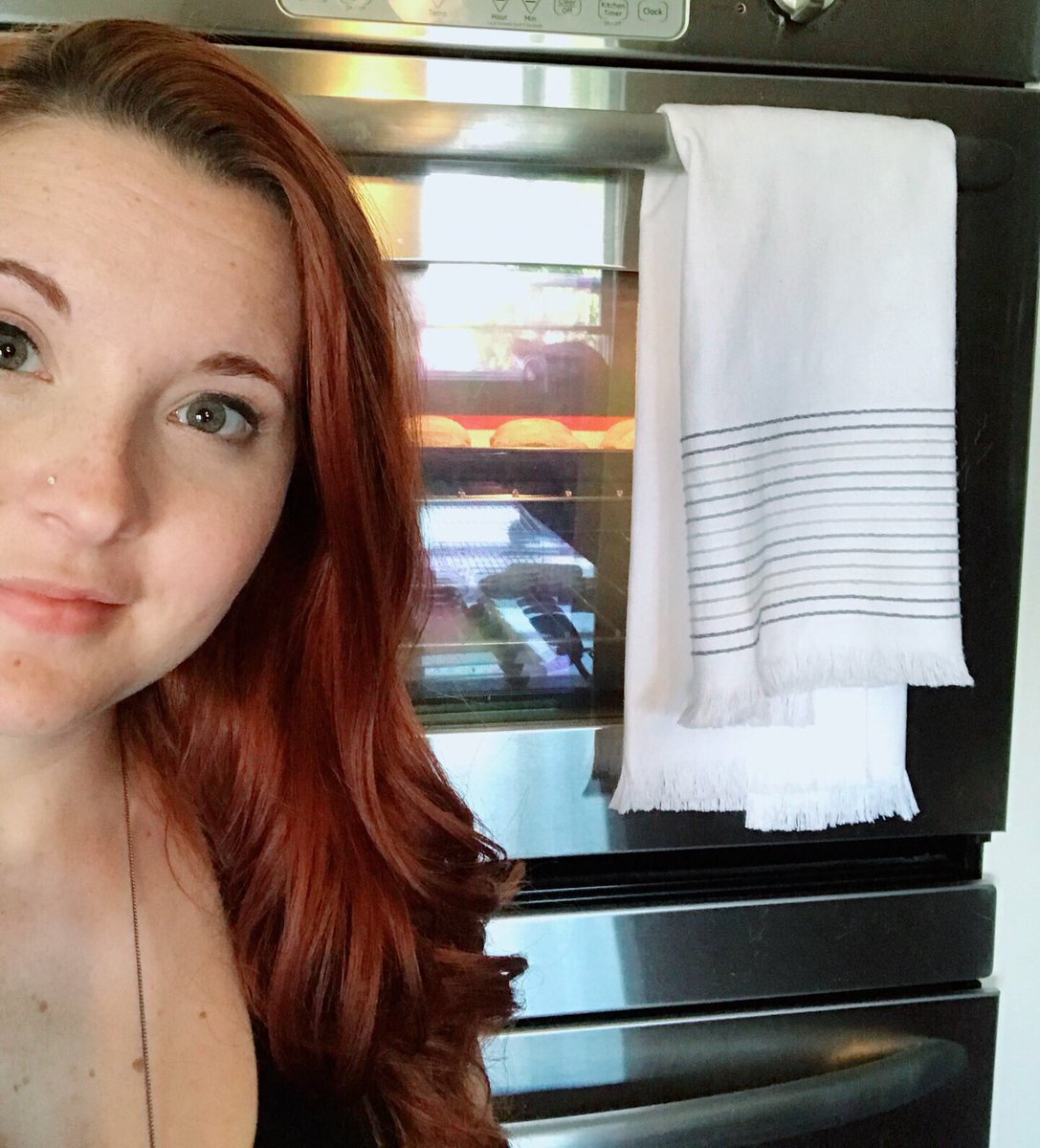 Aureylian in front of the oven, cookies baking inside, reflection of a cat in the window visible in the oven door