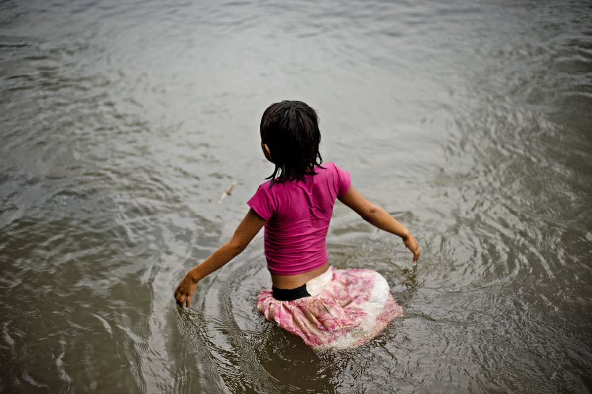 A young girl wades through a tributary of the Amazon in Achuar territory, Ecuador. Oil companies drilling for oil in this region impact the community's way of life and the biodiversity of the rainforest. #Achuar #Amazon #Ecuador
